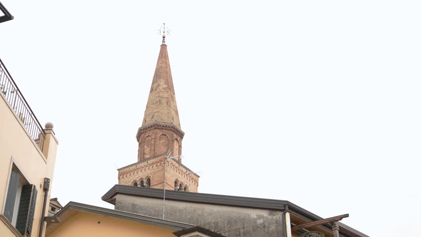 Brick bell tower of Duomo di San Marco rises above yellow houses with wooden shutters in historic center of Pordenone, Friuli-Venezia Giulia region, Italy.