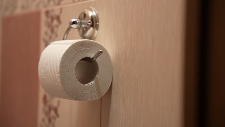 Close-up shot of a white toilet paper roll hanging on a wall-mounted holder in a bathroom. Warm indoor lighting creates a clean and cozy atmosphere. No people visible in the frame. The scene represents everyday hygiene, bathroom essentials, household routine, cleanliness and domestic lifestyle. Suitable for concepts of personal hygiene, home maintenance, bathroom interior, lifestyle content, background footage and practical household themes.