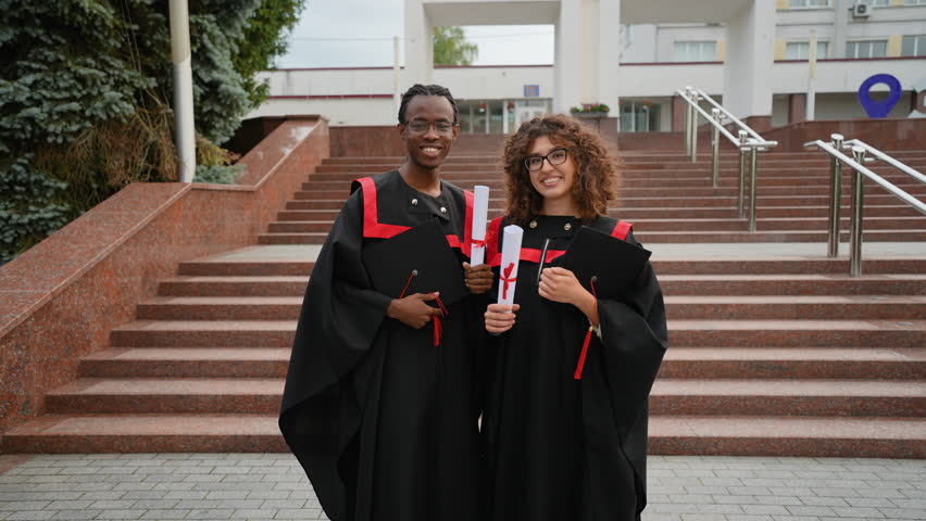 Happy multiracial graduates holding diplomas outside university