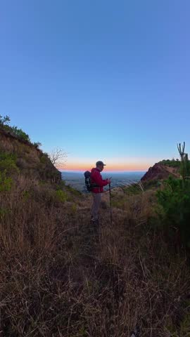 Hiker with backpack and trekking poles checking a smartphone on a hill trail at dawn