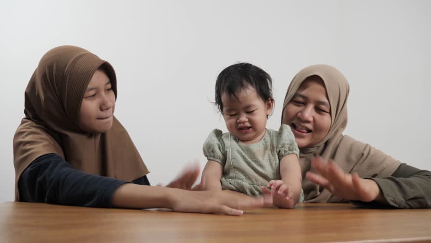 Happy Asian Muslim mother sitting on the floor and bonding with her two daughters