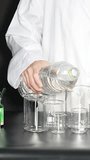 A person in a white lab coat pours water from a bottle into glass beakers. - Powered by Shutterstock - Get 15% off with code: PIKWIZARD15