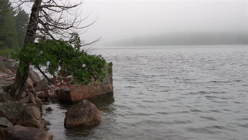 A windy foggy morning on Jordan Pond in Acadia National Park in Maine with the water lapping at the shoreline.