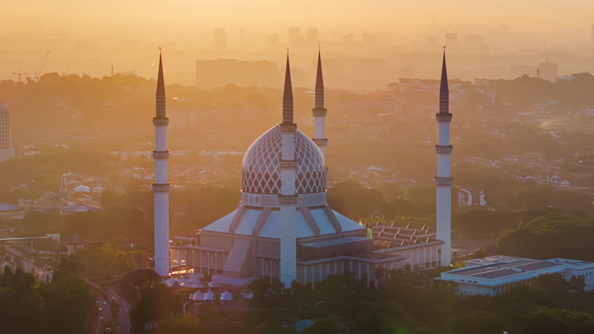 Sunrise time lapse of golden landscape behind Shah Alam and Kuala Lumpur skyline in Malaysia with the Sultan Salahuddin Abdul Aziz Shah Mosque in the foreground.