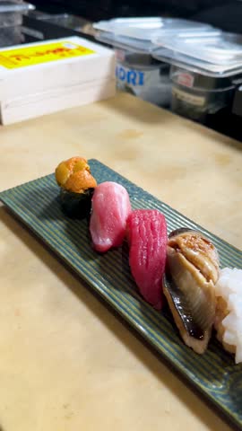 Rotating close-up of assorted nigiri sushi platter on counter under warm restaurant lighting