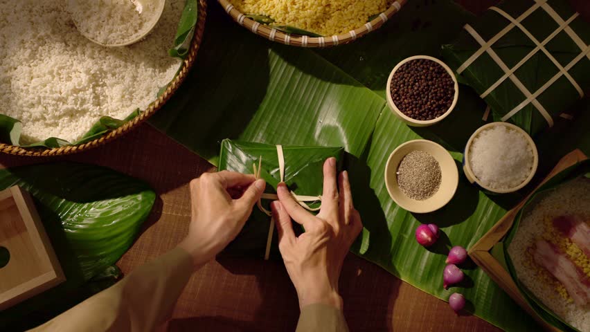 Top view footage of hands tightening dong leaves and shaping chung cake, reflecting skillful traditional Vietnamese food preparation for Tet