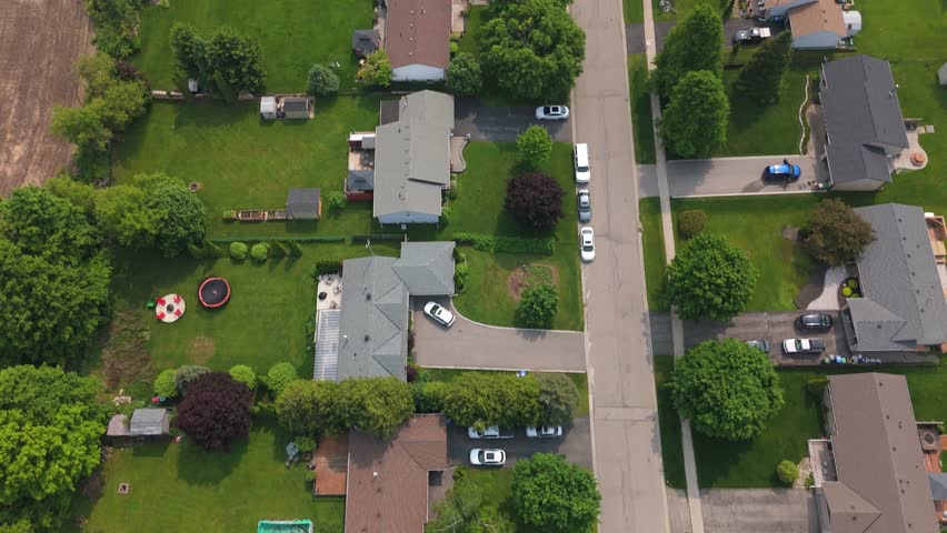 Top-down drone view of a quiet rural subdivision in Caledon, Ontario, Canada with detached houses, large backyards, parked cars, and farmland bordering the street.