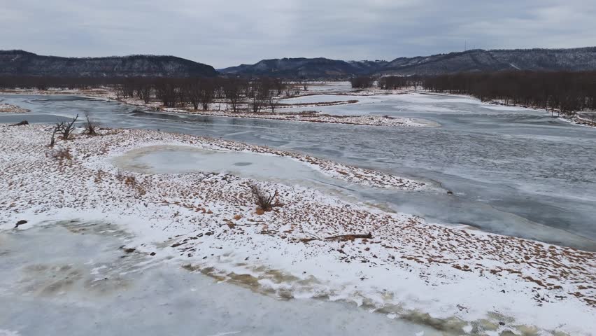 An expansive winter scene features frozen, meandering rivers and scattered islands, framed by dry trees across the Driftless Area.