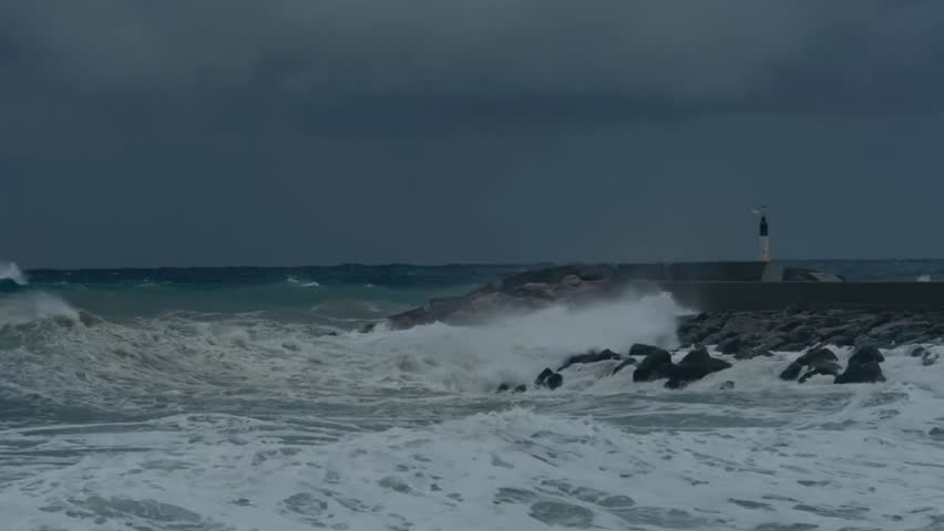 Stormy sea with huge waves crashing against breakwaters under a dark, dramatic sky, showcasing the raw power and hypnotic beauty of nature.