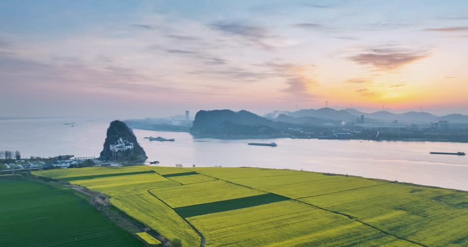 Aerial time-lapse of sunrise over golden rapeseed fields at Xiaogu Hill, with the Yangtze River and busy water transport scene. Stunning natural and rural landscape, Anhui Province, China.
