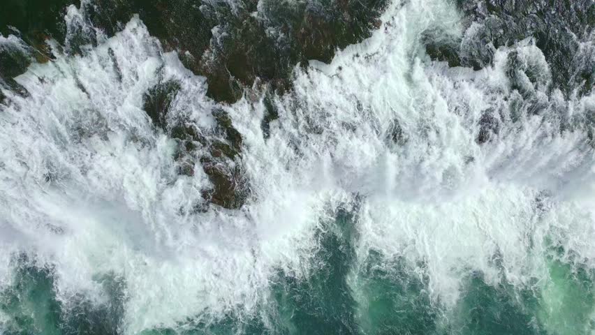 Top-down aerial shot of a large Icelandic waterfall with rushing water and foam, with green and transparent water, showcasing the raw beauty of Icelandic nature