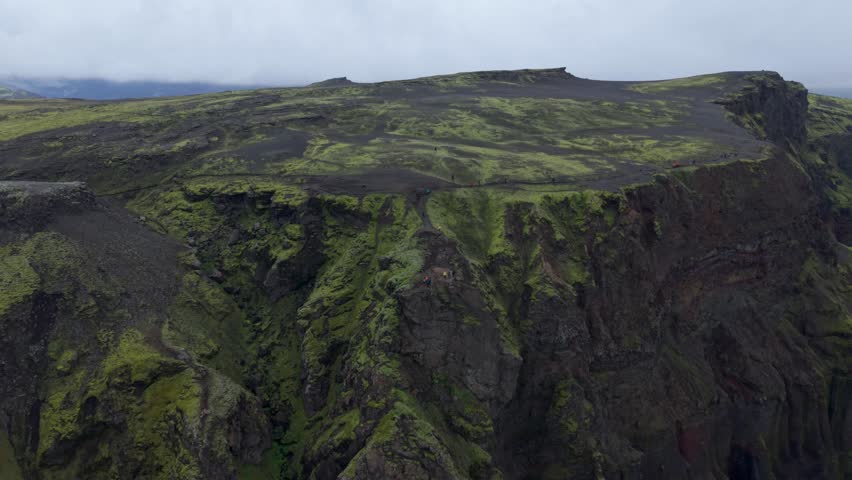 Aerial view of mossy volcanic plateaus and steep cliffs under a heavy mist. Flying back.