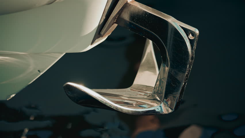 A chrome boat anchor with smooth curves, set against abstract blue and turquoise water reflections in a marina