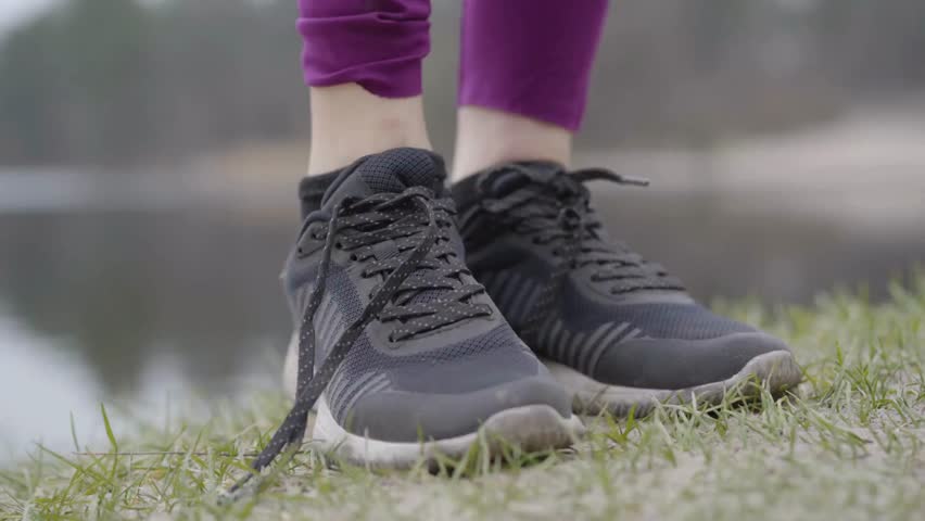 Close-up shot of female athlete preparing for training, running or exercising. female hands tying her sneakers shoelaces. Young woman in sport wear tying shoelaces outdoors.