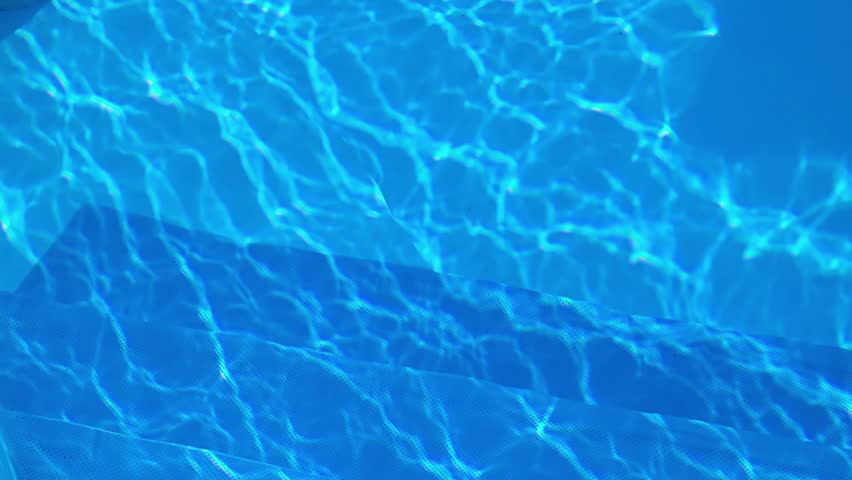 Bright sunlight creating caustic patterns on the rippling surface of a swimming pool, casting beautiful shimmering light reflections and refractions on the textured blue pool floor