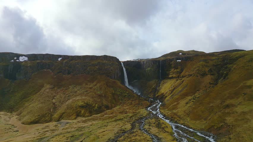 Aerial drone view of an Icelandic waterfall within a cliff on a cloudy day. Cinematic landscape showcasing dramatic Nordic nature and untouched wilderness.
