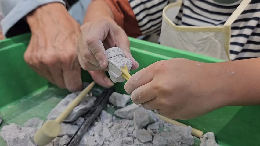A happy child digs up a dinosaur and have fun with archaeological excavation equipment. A boy and his grandfather play archaeologists, digging and practicing digging up fossils. 4K Video