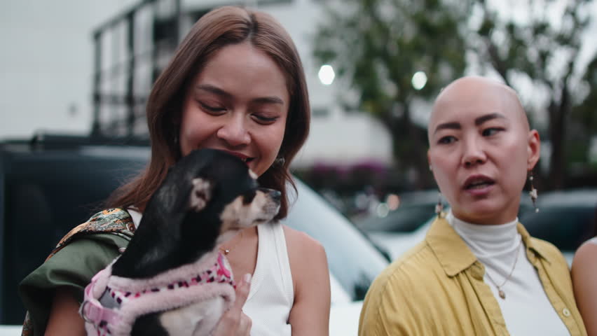 Two asian women playing with a small chihuahua dog outdoors