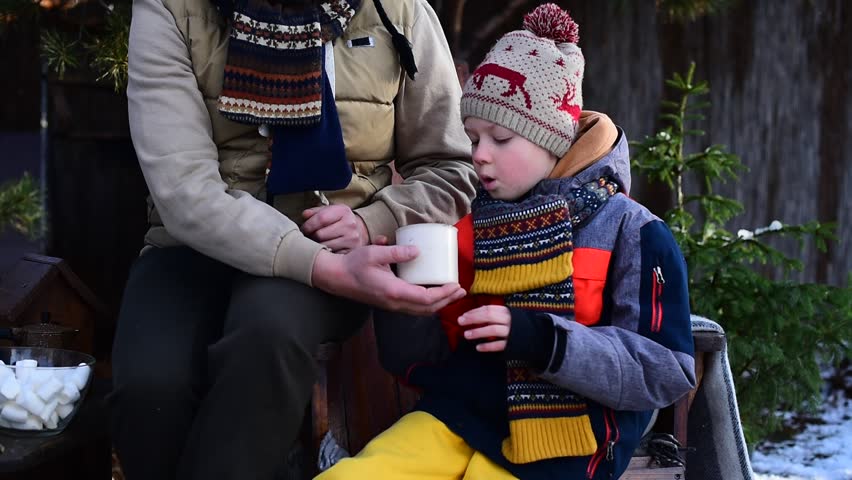 Pre-teen boy drinking hot tea from a mug near his father in the yard in winter