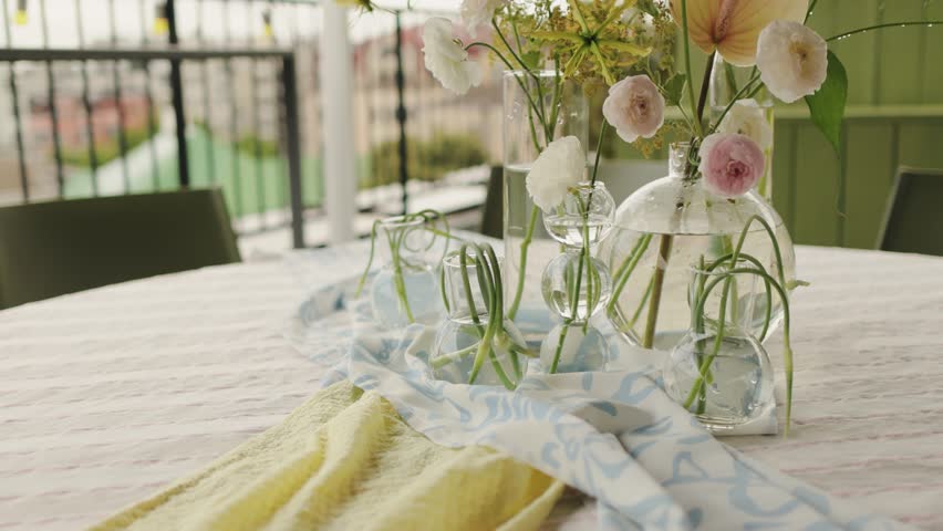 pastel bud vases on outdoor balcony table with view, stylist arranging napkins and ribbons, relaxed brunch