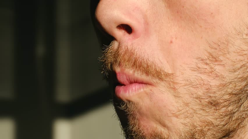 Sunlit closeup of man, Unshaven man biting gum indoors, Quiet scene showing nervous man chewing gum in sunlight, Reflective mood as man with unshaved jawline chews gum quietly indoors