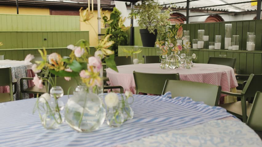 glass vases and loose blooms on striped tablecloth with pink linen in background, venue setup for rehearsal