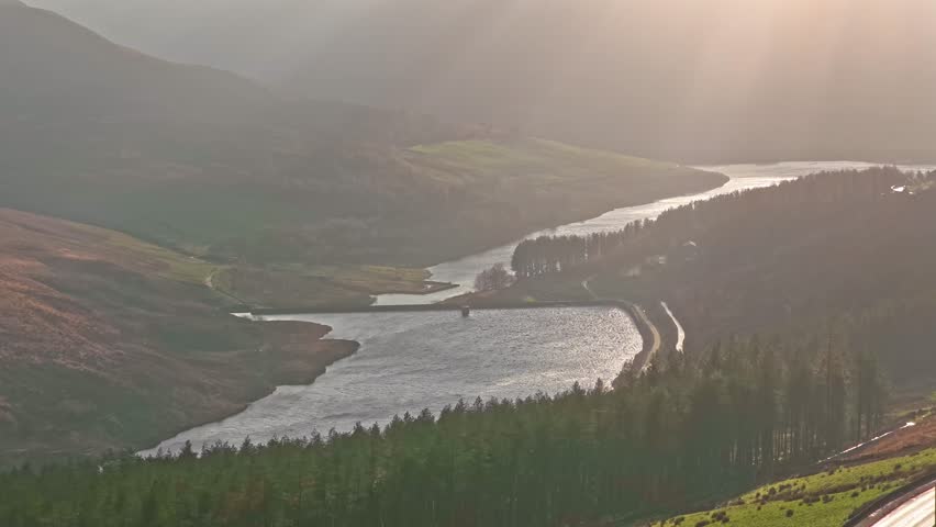 Static aerial drone frames Dovestones Reservoir landscape with winding water body conifer forest dense green vegetation moorland slopes overcast sky Peak District Saddleworth geology.​