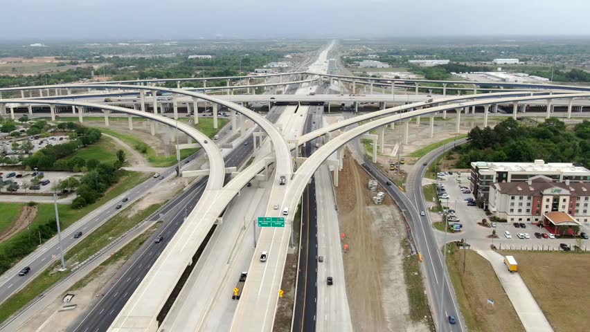 Aerial view of a complex highway interchange, where ribbons of concrete interweave, creating a network of roads amidst green spaces, Houston, Texas, United States.