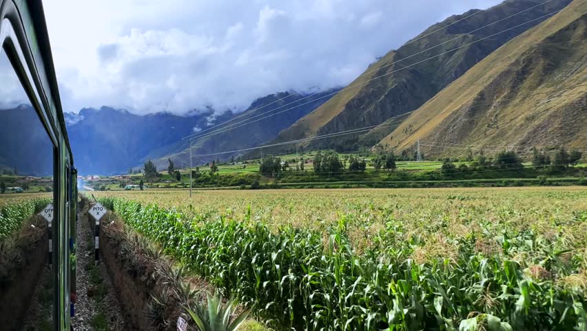 Ollantaytambo in route Aguas Clients Amazon Urubamba river Peru Rail train farm lands corn fields land Inca Trail Machu Picchu Peruvian Andes mountains range peaks rainy season sunny blue sky clouds