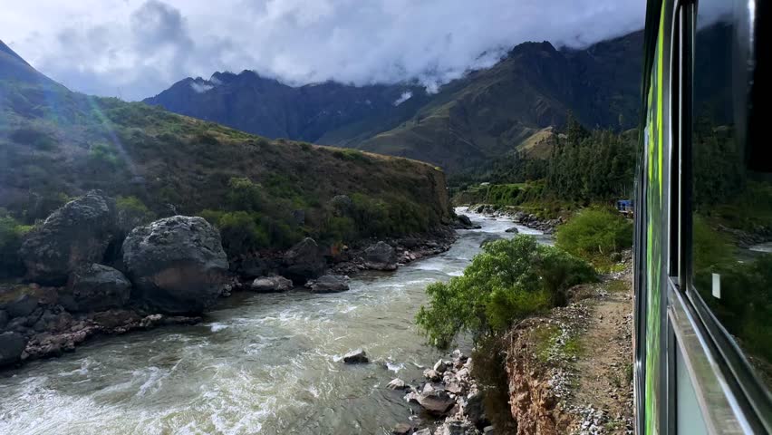 Peru Rail train Urubamba river high flow Inca Trail Ollantaytambo in route Aguas Calientes Machu Picchu Peru Peruvian Andes mountains range peaks rainy season sunny flare blue sky cloudy forwards