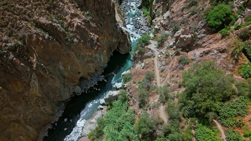 Bird’s-eye drone flyover captures Rio Colca’s vivid rapids and iconic suspension bridge The zigzag hiking trail and surrounding canyon highlight human ingenuity and life in rugged Colca Canyon terrain