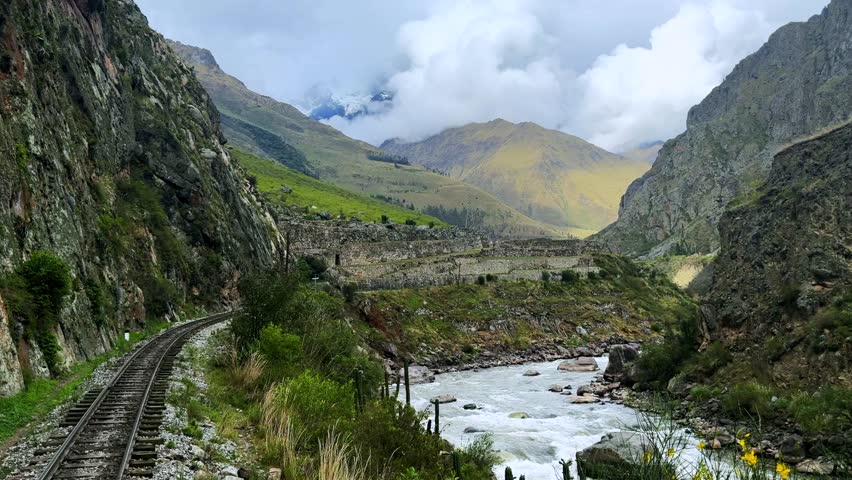 Peru Rail train tracks Inca Trail Ollantaytambo in route Aguas Clients Amazon Urubamba river Machu Picchu Peruvian Andes mountains range peaks rainy season sunny blue sky clouds power lines backwards