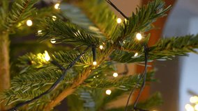Sharp close-up of fir branches wrapped with warm micro LED fairy lights, dark cable visible, cozy indoor holiday decor with soft bokeh in the background. - Powered by Shutterstock - Get 15% off with code: PIKWIZARD15