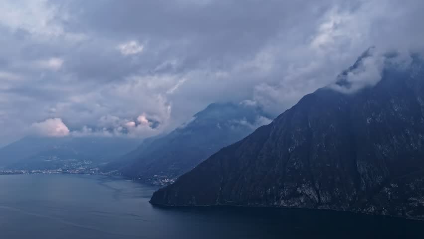 Static drone timelapse showing clouds moving above mountains and a calm lake.