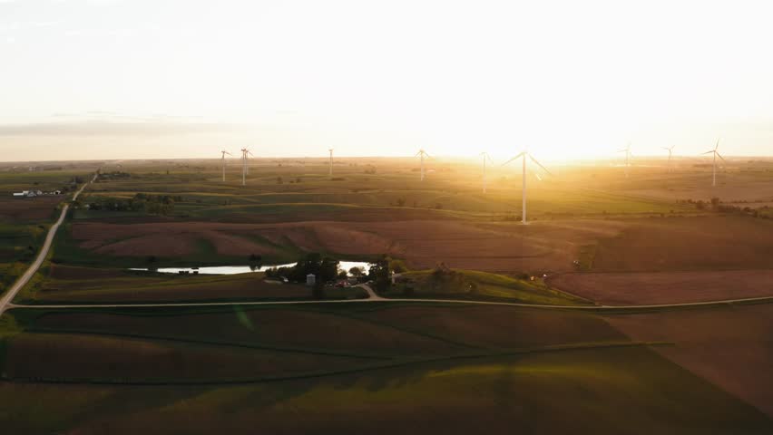 Wide aerial shot of a windmill farm in Iowa with the sunsetting behind them as they turn.