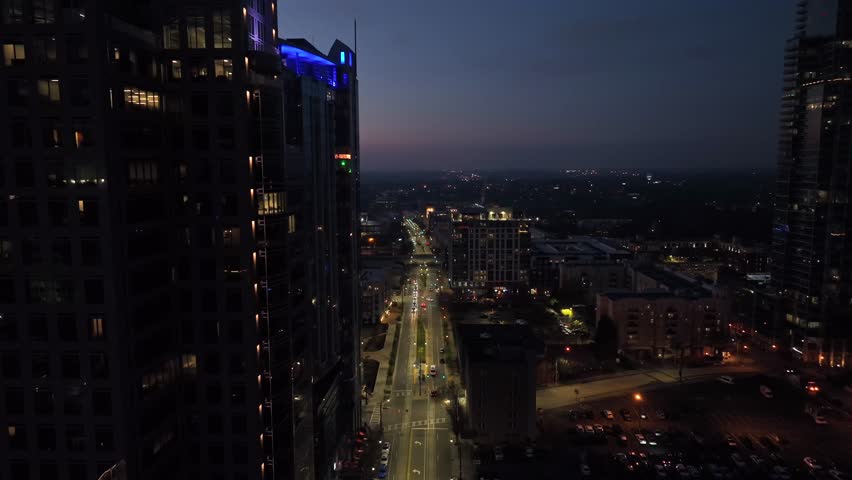 Main Street of Charlotte Downtown at dusk. Lighting skyscraper and residential towers complex of american town. Aerial descend wide shot.
