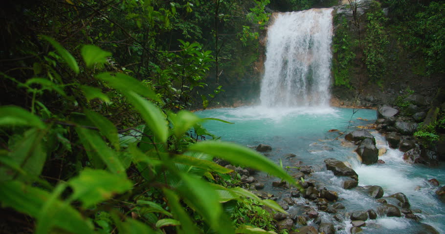Blue Falls waterfall cascades into a vibrant turquoise pool surrounded by rainforest scenery in Costa Rica