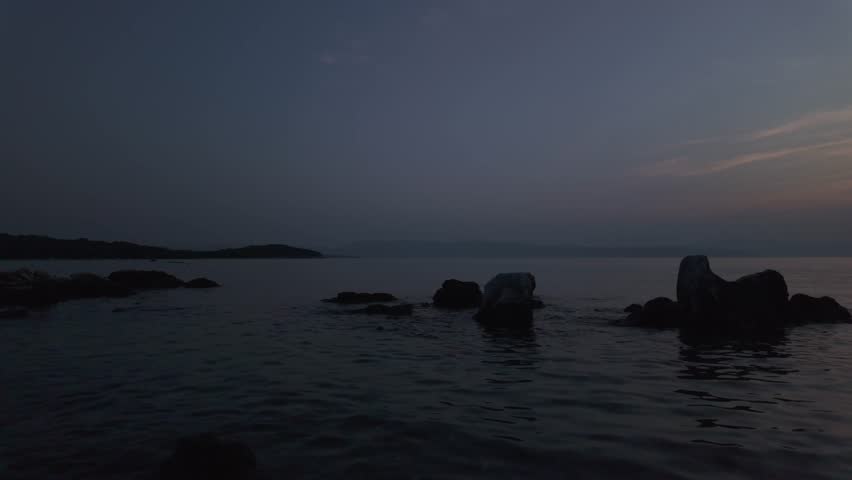 Real time tranquil sunset above the Adriatic Sea with original sound of continuously waving water. Evening view from Njivice - Krk Island, Croatia with huge rock formations in the foreground.