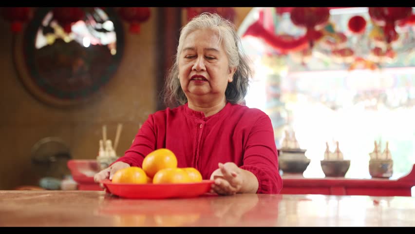 Elderly thai woman chinese descent dressed in red offers oranges as an offering to the gods praying happiness prosperity wealth and good health chinese temple during the chinese New Year festival.