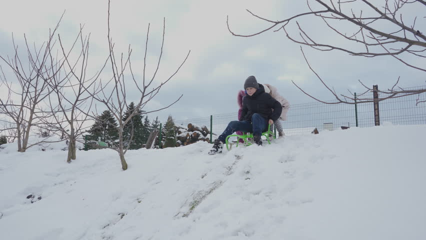 two little girls pushing a sled with a boy down a snowy hill, a boy sledding down a hill and two little girls on the hill, winter children