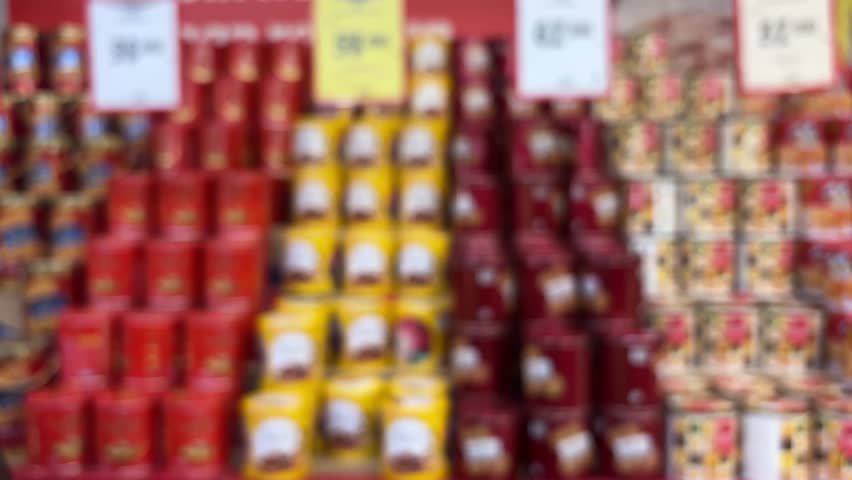 Blurred or defocused image of a woman choosing biscuits at a supermarket. Background: a pile of biscuit tins for Eid needs.