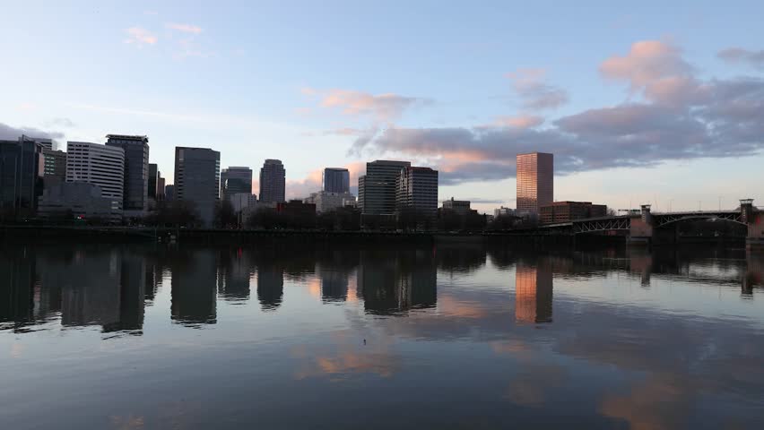 4K timelapse video of Downtown Portland Oregon captured at sunset with the Willamette River in the foreground. City skyline buildings reflect in calm water as light changes over time, with the Burnside Bridge visible across the river. Clean urban landscape ideal for city identity projects, business and corporate media, travel promotion, metropolitan visuals, time passing concepts, presentation backgrounds, marketing content, and professional motion footage.