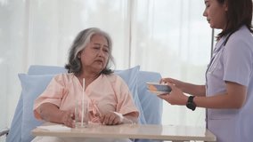 Young Asian nurse feeding breakfast to senior woman patient on bed in hospital ward, elderly care concept. - Powered by Shutterstock - Get 15% off with code: PIKWIZARD15