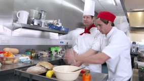Time lapse clip of a busy team of chefs, working hard and preparing food in a commercial or restaurant kitchen. One male chef stands frozen in time while his colleagues bustle around him.