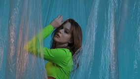 Portrait of a young female model in a green top, posing against a blue background with transparent plastic curtains. Color beauty, fashion art. - Powered by Shutterstock - Get 15% off with code: PIKWIZARD15