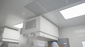 Cleanroom technician working beneath a laminar flow hood with HEPA filtration, inspecting racks and components in a sterile laboratory environment for precision manufacturing - Powered by Shutterstock - Get 15% off with code: PIKWIZARD15