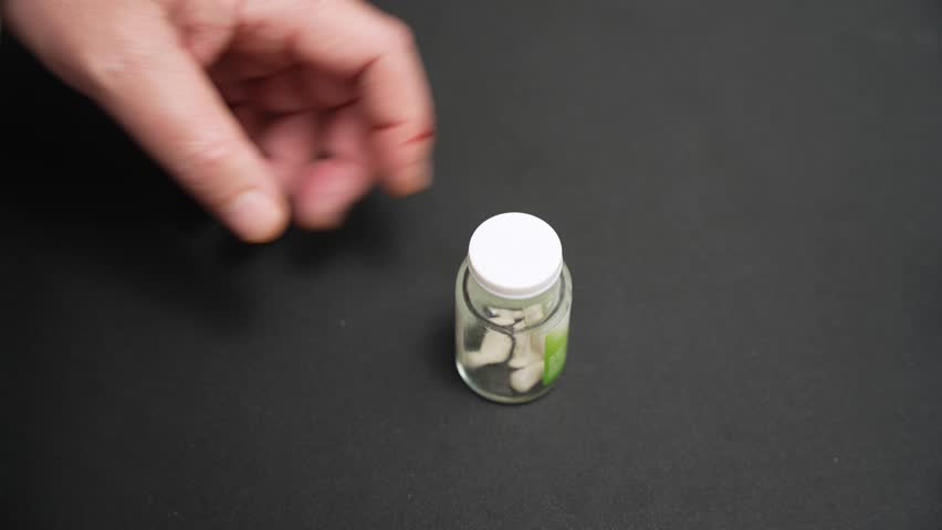Pouring pills from bottle. Close-up video of pills being poured from a small bottle into a hand. Medication dosage and pharmaceutical concept.