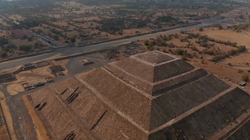 Tilt-up aerial of ancient Mesoamerican pyramids in Teotihuacan, Mexico, revealing massive structures and dry landscape of this historic archaeological site.