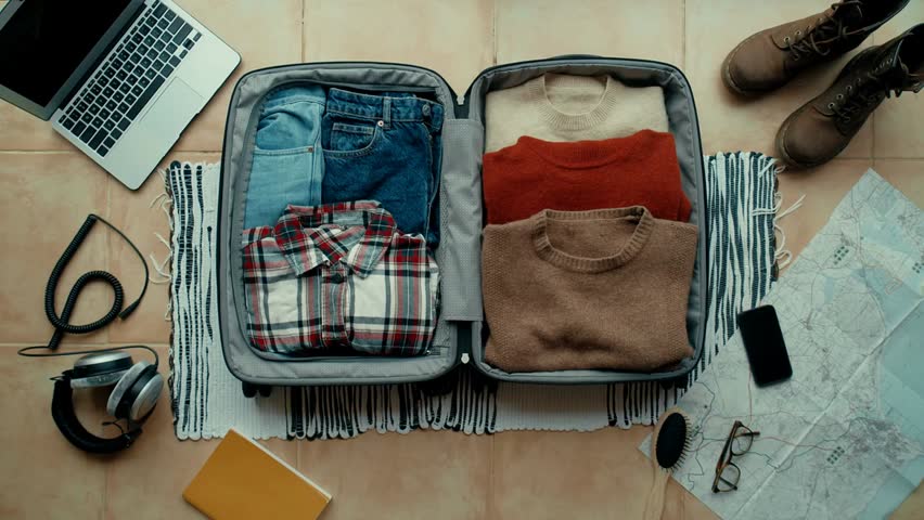 Woman carefully packs a winter-themed suitcase for an autumn holiday, featuring travel essentials, social media props, and a vintage camera for her journey.