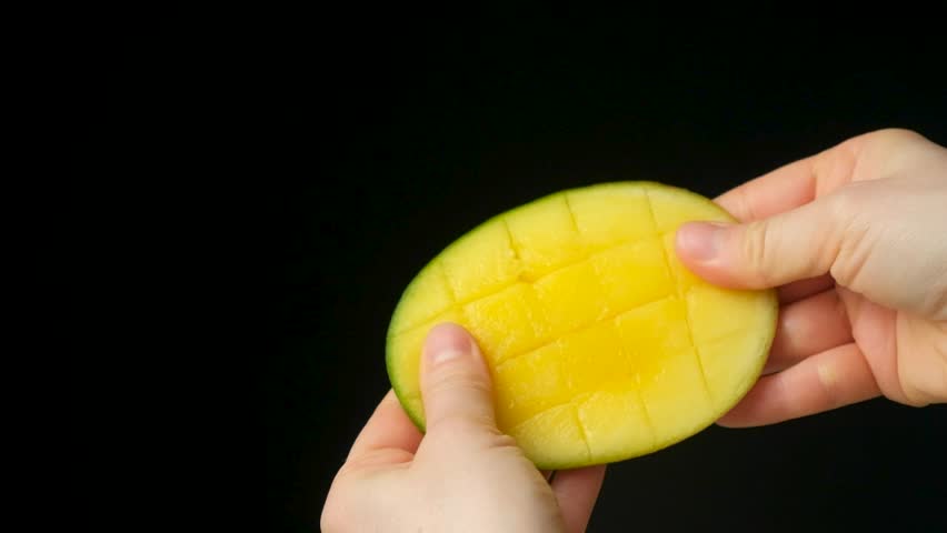 Hands showing and opening a fresh diced half of a mango fruit.